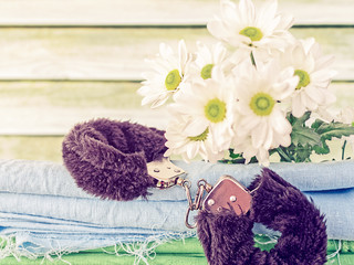Fur handcuffs for sex games and a bouquet of white chrysanthemums are on a blue linen fabric with untreated edges. Below is a green textured napkin. Wooden background.