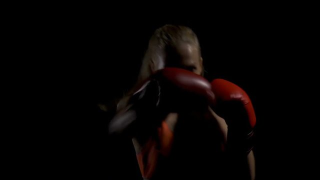 Young female kickboxer shadow boxing as exercise to training for the fight. Boxing in the darkness. 