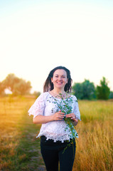 happy young beautiful brunette girl with  bouquet wild flowers hands in the field. on open air. summer sunset