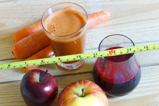 Fresh, homemade carrot and beet juice in a glass with carrots and apples on wooden background and measuring tape. Dieting and healthy eating concept.