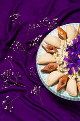 Novruz celebration plate with traditional national pastries in Azerbaijan - shekerbura and pakhlava decorated with spring  flowers daffodils and purple fleur de lis silk purple background copy space