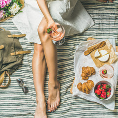 French style romantic picnic setting. Woman in dress with glass of wine, strawberries, croissants, brie cheese, sunglasses, peony flowers on blanket, top view, square crop. Outdoor gathering concept