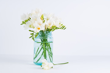 white fressia flowers in a blue glass jar on a white background