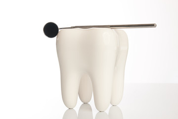 Tooth model and dental mirror. Ceramic tooth and dentist equipment, steel dental mirror tool isolated on white background with copy space, close-up. Dentist stomatology medical concept 