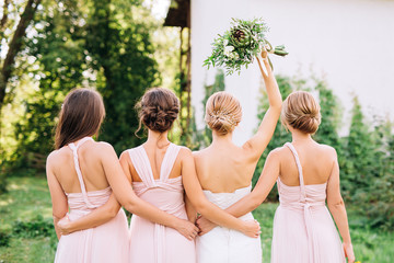 bride standing with her back  and raised hand with a bouquet  in the embraces of three bridesmaids in pink dresses transformer  - obrazy, fototapety, plakaty