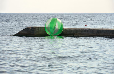 Obraz premium Green transparent water ball is in the sea near groyne.
