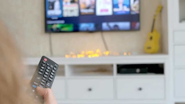Hand hold TV remote control. TV on the background.