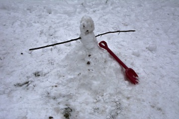 A terrible and ugly snowman made by children in the winter courtyard of a private house on the day of vacation and festive mood against the background of white and dirty snow.
