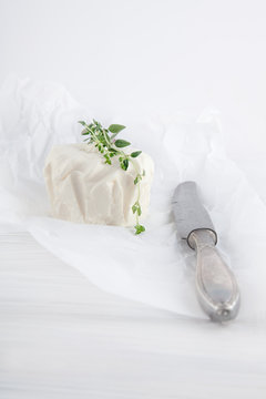 fresh cream cheese with knife and oregano on white paper and white wood table can be used as background