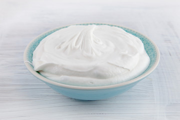 Bowl of fresh whipped cream on white wooden table can be used as background