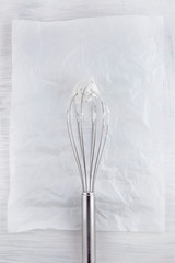 whisk with freshly prepared whipped cream on white wooden table can be used as background