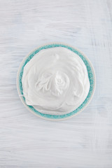 Bowl of fresh whipped cream on white wooden table can be used as background