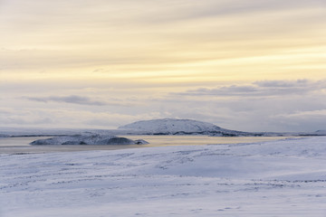 Hills (mountains) in the middle of Thingvallavatn lake in Iceland. Snow fields in the foreground, yellow overcast skies in the background.