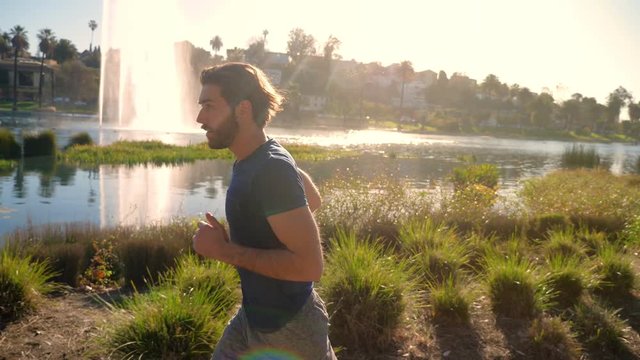 Athletic man jogs around a small lake in Los Angeles. Buildings of Los Angeles skyline can be seen in the distance.
