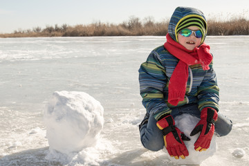 Happy boys in colorful winter clothes doing gymnastics on ice and snow. Glasses for skiing, snowboarding and sledging. A child is playing outdoors in the snow. Outdoor fun for winter holidays