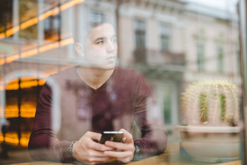 The man sitting with a phone over the window in a cafe