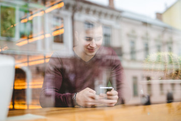 The happy man sitting with a phone over the window in a cafe