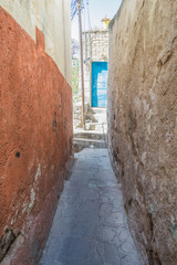 A very narrow stone passageway with a stone wall on one side, and an orange and yellow wall on the other, at the end, a blue door, in the UNESCO World Heritage Site, Guanajuato - 192073908