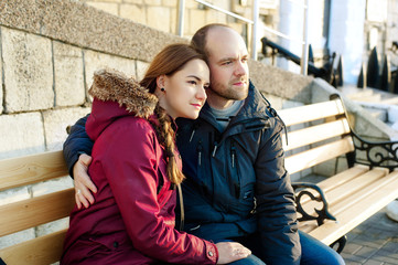 Happy loving couple hugging in city. Portrait of young attractive smiling man and woman relaxing on a warm winter day on a bench