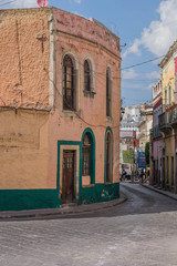A street scene with a curve corner building painted yellow and green, a cobblestone street and other architectural details, in Guanajuato, Mexico - 192074351