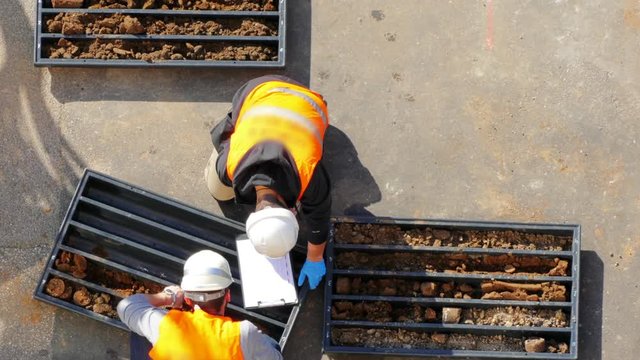 rilling rig workers. Two industrial men examining soil, writing down the dates and sorting it into two black plastic boxes. Drilling process. Energy and power. Modern machinery