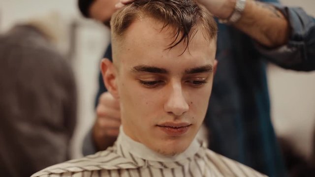 Haircut in barbershop. Moustached Barber cuts young client.
