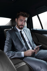 Fototapeta na wymiar man in suit sitting in car and reading messages on smartphone
