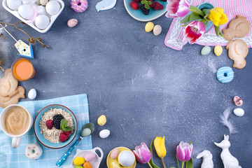 Delicious spring breakfast on a gray stone background. A bouquet of fresh tulips of pink and mint color. Small and large colored easter eggs. Oatmeal, biscuits, coffee and juice. Postcard and place fo