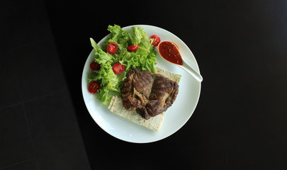 Grilled steak served with tomatoes, salad, hot sauce and thin pita bread
