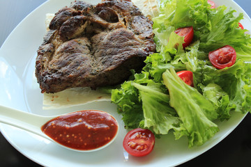 Fried meat and spicy sauce served on plate with lettuce leaves and thin bread
