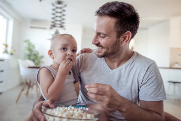 Happy father and little son with popcorn at home.