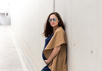 portrait of young pregnant lady with sunglasses posing near concrete wall