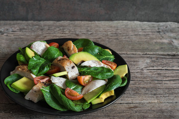 Chicken salad with avocado, spinach and tomatoes cherry in black plate