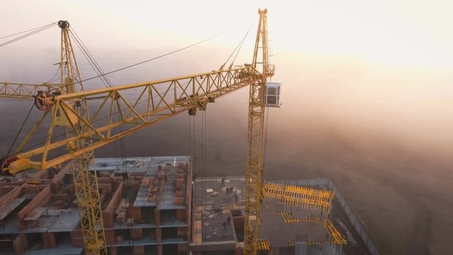 Construction site in the fog with a bird's eye on the Sunset. Aerial Video . Tower crane, excavator and sand. Flying over the construction site. The construction of the plant in the city.