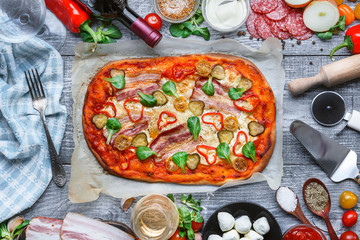delicious Italian traditional pizza on a wooden background with ingredients and a bottle of red wine