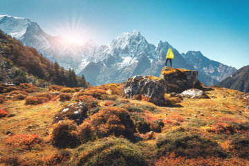 Stehender Mann auf dem Stein und Blick auf die erstaunlichen Himalaya-Berge bei Sonnenuntergang. Landschaft mit Reisenden, hohen Felsen mit schneebedeckten Gipfeln, Pflanzen, Wald im Herbst in Nepal. Lebensstil, Reisen. Wandern