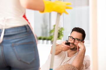 Woman mopping floor while man watching tv