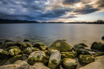 Steine am schönen Seeufer des Bodensees zum Sonnenuntergang mit kraftvollen Wolken am Himmel