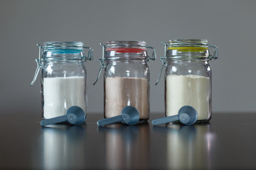Three glass jars with protein powder, strawberries, banana and chocolate and three scoops for milkshakes. Sports and dietary nutrition for athletes and weight loss or muscle mass bodybuilders.