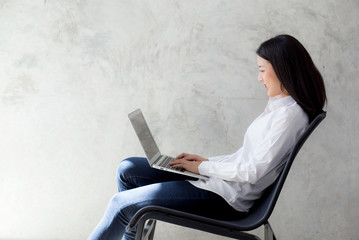 Beautiful asian young woman working online on laptop sitting at cement background, professional female freelancer using notebook computer with connect to internet for distance job.