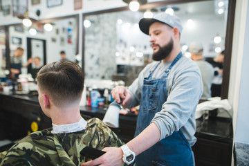 A stylish barber with a beard finishes a male hairstyle to the client. Men's haircuts in barbershop. Young handsome barber making haircut of attractive man in barbershop