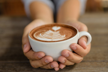 Woman hands holding cup of hot coffee latte cappuccino with heart shaped. Love, Wedding and Valentines day concept.