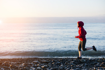 Adult woman runner running on sunrise seaside. Healthy lifestyle.