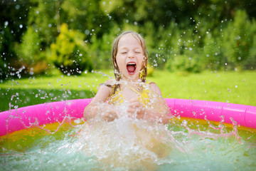 Adorable little girl playing in inflatable baby pool. Happy kid splashing in colorful garden play center on hot summer day. © MNStudio