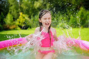 Adorable little girl playing in inflatable baby pool. Happy kid splashing in colorful garden play center on hot summer day. © MNStudio