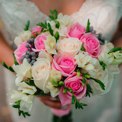 wedding beautiful bouquet with delicate white and pink roses in the hands of the bride on the background of the dress