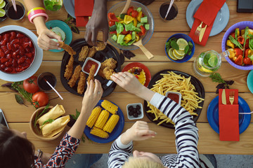 Top view of group of people having dinner together while sitting at wooden table. Food on the table. People eat fast food.