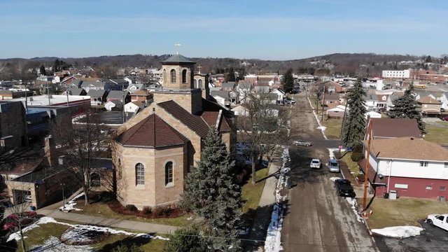 A slow push forward aerial establishing shot of a church in a typical Western Pennsylvania residential neighborhood. Pittsburgh suburbs.  	