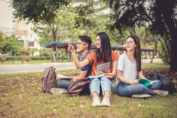 Group of Asian college student reading books and tutoring special class for exam on grass field at outdoors. Happiness and Education learning concept. Back to school concept. Teen and people theme.