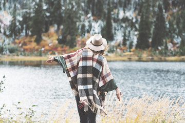 Stylish woman traveling among mountains, forest and lake wearing hat and poncho, boho and...